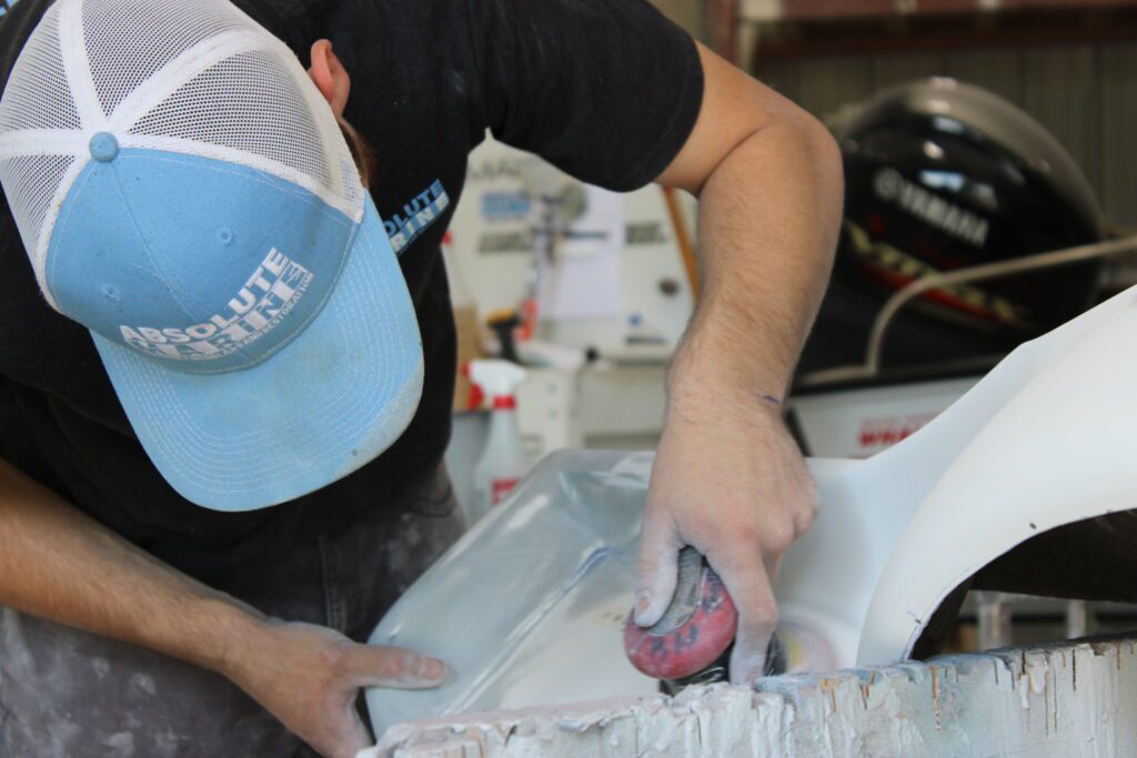 Close up shot of man leaning down wearing blue Absolute Marine hat, working on boat.