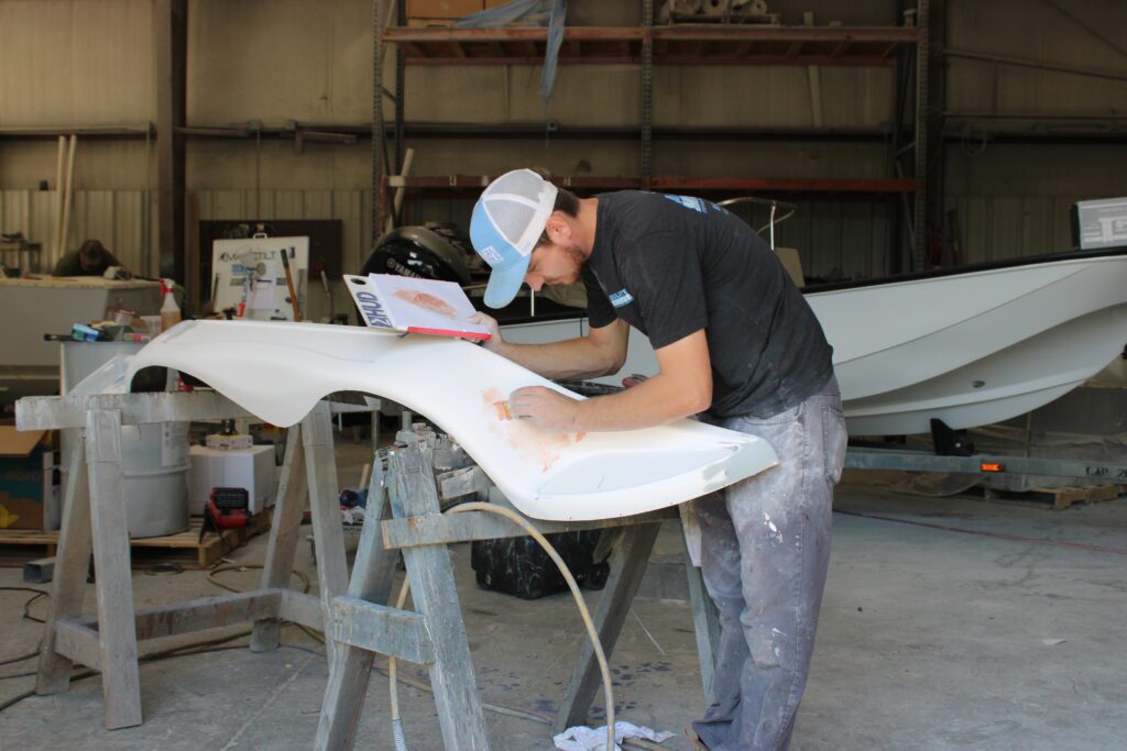 Man dressed in Absolute Marine shirt, Absolute Marine hat, and jeans working closely on a boat.